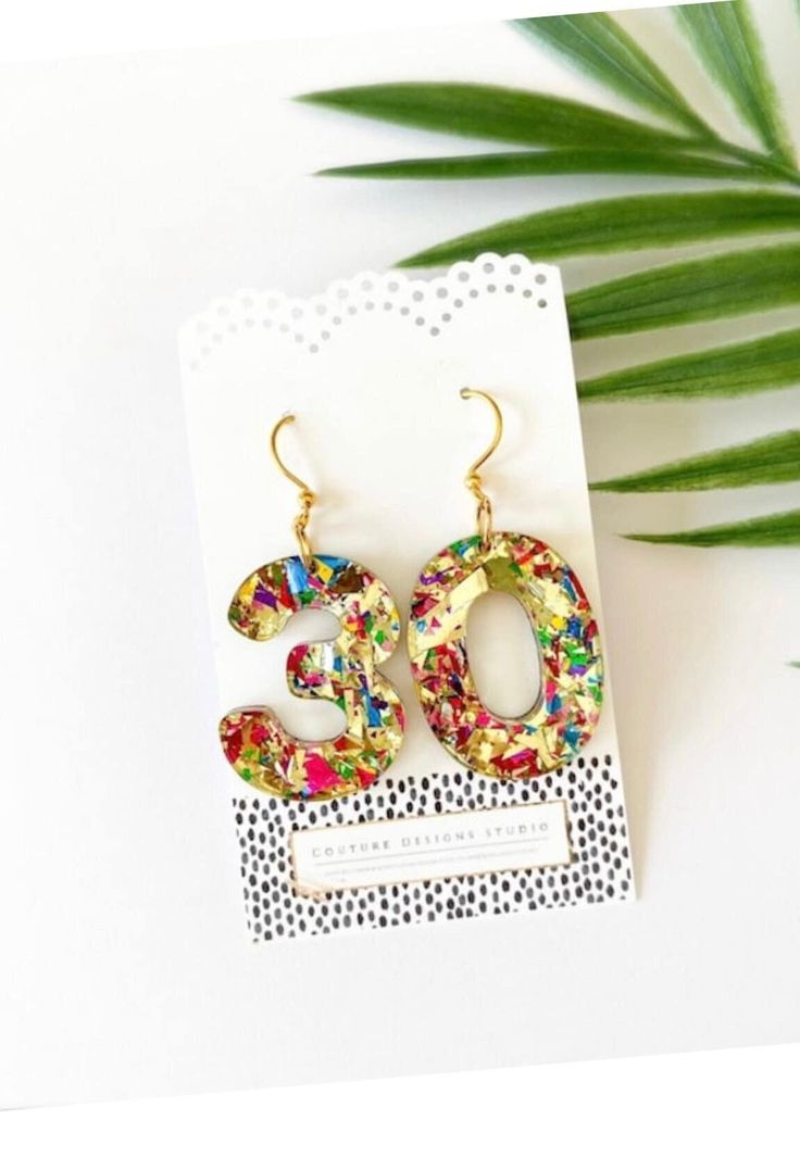 a pair of colorful earrings sitting on top of a white card next to a plant