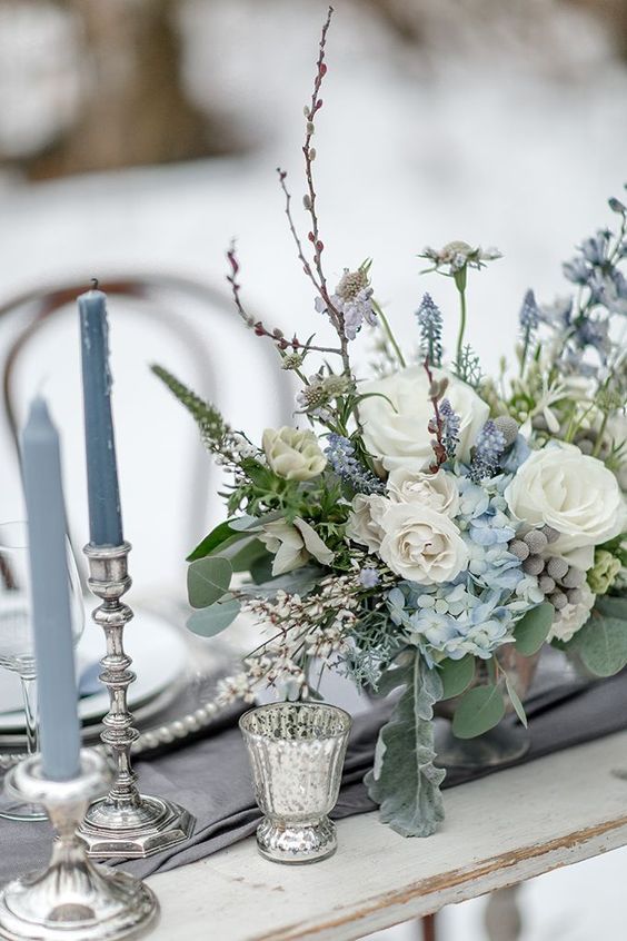 a table topped with a vase filled with blue and white flowers next to two silver candles