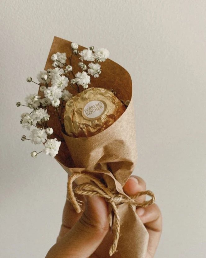 a hand holding a bouquet of flowers wrapped in brown paper