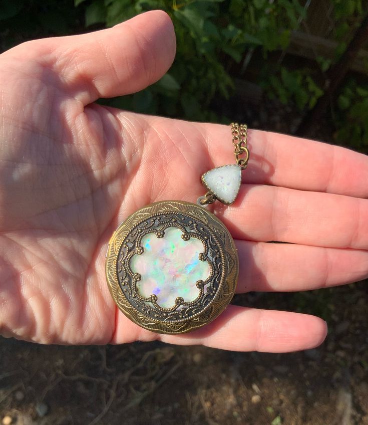 This beautiful locket is made with Baroque and Rococo eras in mind.  The bronze plated copper has been antiqued to bring out intricate details. The center carefully made to look like a blue iridescent moonstone or opal.  It is framed by a scalloped lace edge Victorian style medallion.  The light dances over it and the colorful flash is amazing. It is connected to an 18 inch bronze chain with a triangle bezel. The locket opens up to hold your special treasures inside.   This is a beautiful gift f Vintage Medallion Jewelry For Festival, Vintage Medallion Jewelry For Festivals, Vintage Festival Medallion Jewelry, Bohemian Antique Gold Brass Locket Necklace, Bronze Brass Jewelry Keepsake, Bohemian Engraved Round Locket Necklace, Handmade Round Brass Locket Necklace, Bohemian Brass Locket Necklace With Vintage Charm, Antique Gold Bohemian Medallion Locket Necklace