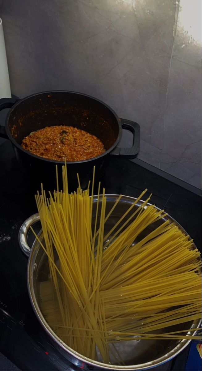 two pans filled with spaghetti on top of a stove next to a white candle