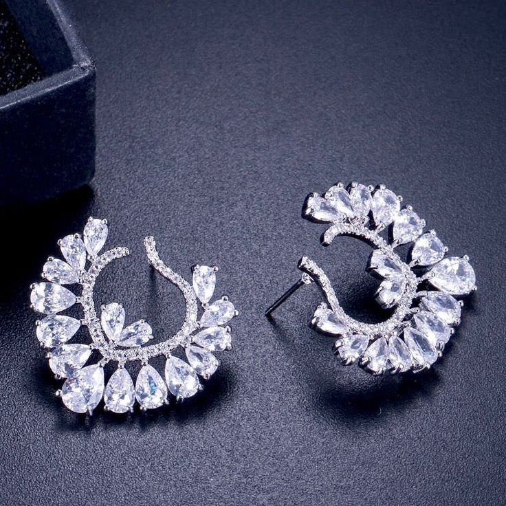 A unique pair of bridal earrings with an incredible sparkle! Adorned with flawlessly faceted cubic zirconia that capture the light from every angle with a perfectly translucent appeal, the earrings are rhodium plated for a bright finish which enhances the intricate detailing and conveys a modern take on old elegance. Overall length of the earring is 1.2" (approx. 3cm). Width: 1" (approx. 2.5cm). Weight: 8.6g. Hypoallergenic - lead, nickel and cadmium free. This exquisite design will add a touch Cubic Zirconia Bridal Earrings, Popular Earrings, Silver Wedding Jewelry, Bridal Jewelry Set, Flower Stud Earrings, Flower Stud, Flower Earrings Studs, Party Jewelry, White Earrings