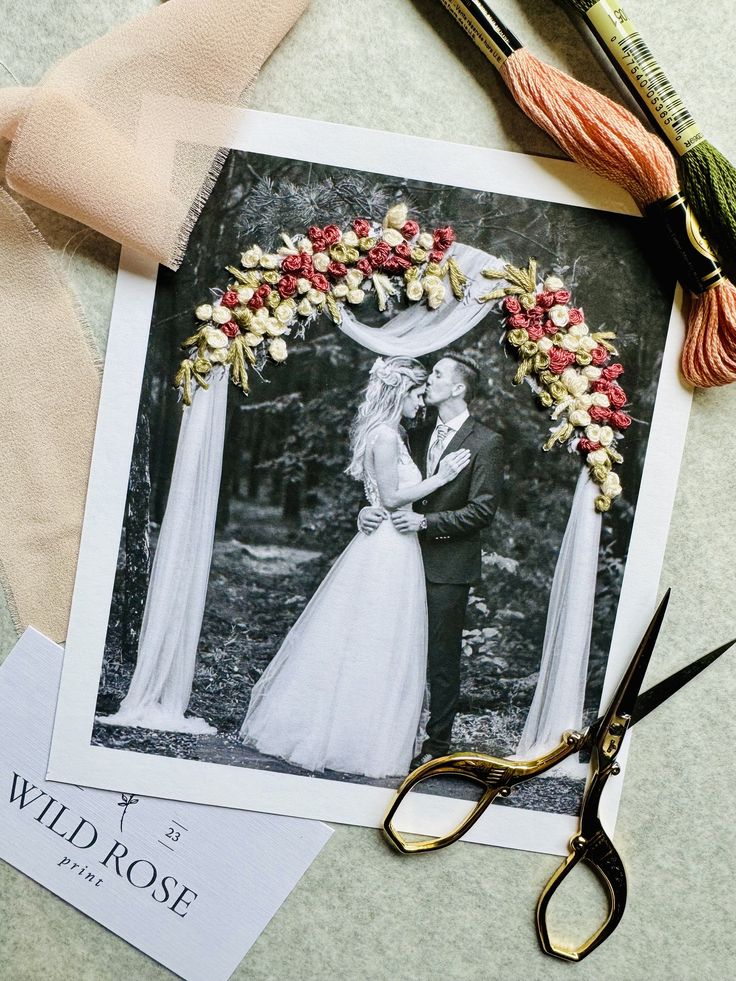 an old photo and scissors are laying on the table next to each other, with some flowers in front of it