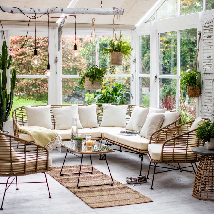 a living room filled with lots of furniture next to a large glass window covered in potted plants