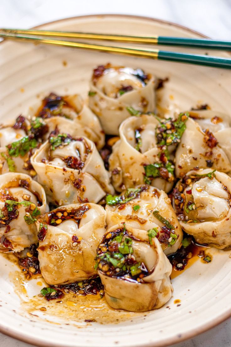 a white plate topped with dumplings covered in sauce and garnished with green onions