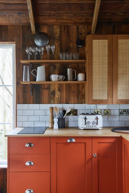 a kitchen with red cabinets and white tile backsplashing, wooden shelves above the sink