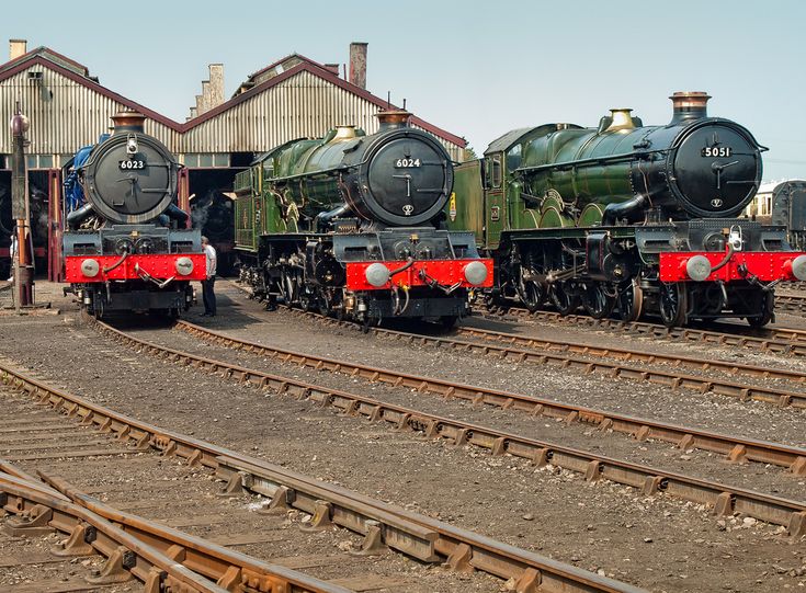 three trains are parked on the tracks in front of some buildings and one is green