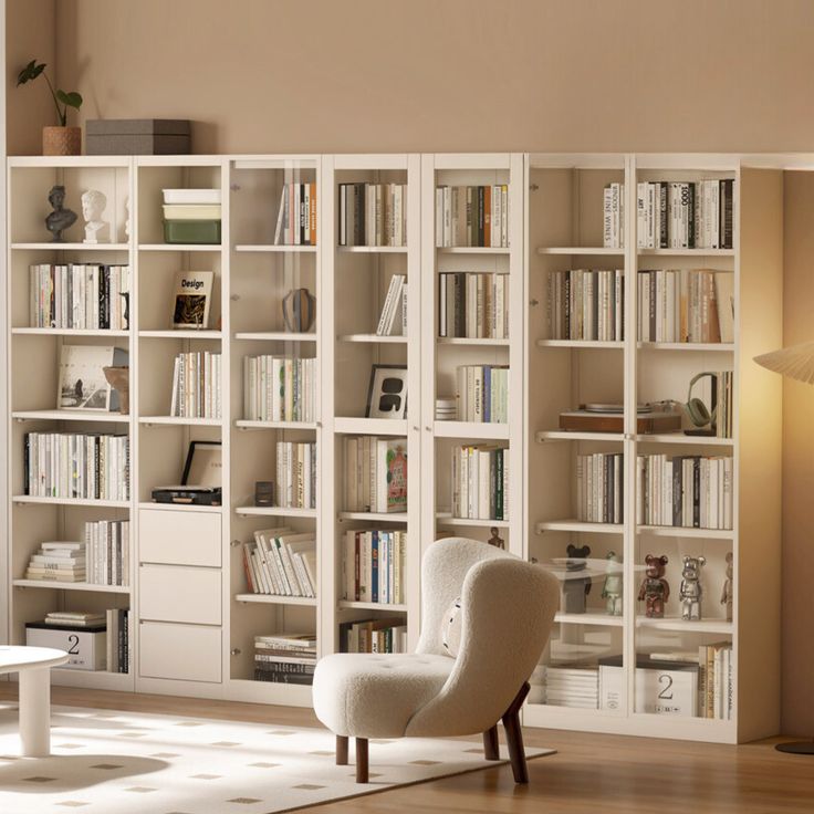 a white chair sitting in front of a book shelf filled with lots of books next to a lamp