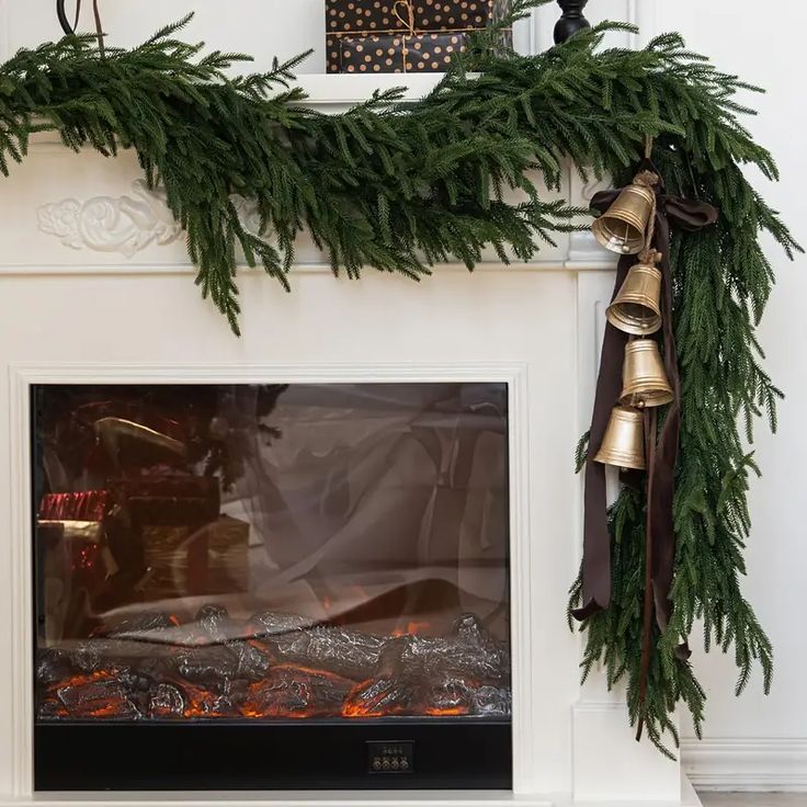 a fireplace decorated for christmas with bells and greenery on the mantel above it