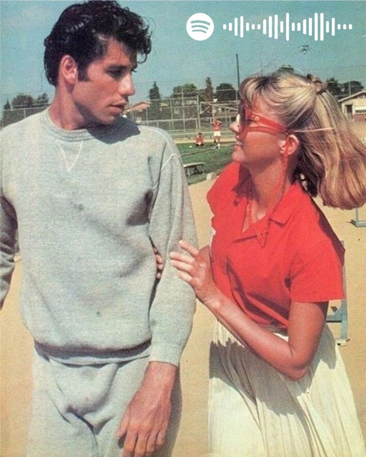 a man standing next to a woman on top of a sandy beach