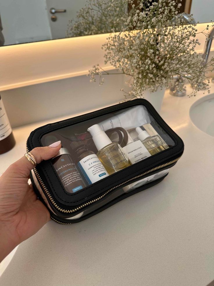 a person is holding a black case filled with personal care products in front of a bathroom sink