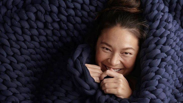 a woman is smiling while wrapped in a blue blanket with her hands on her chin