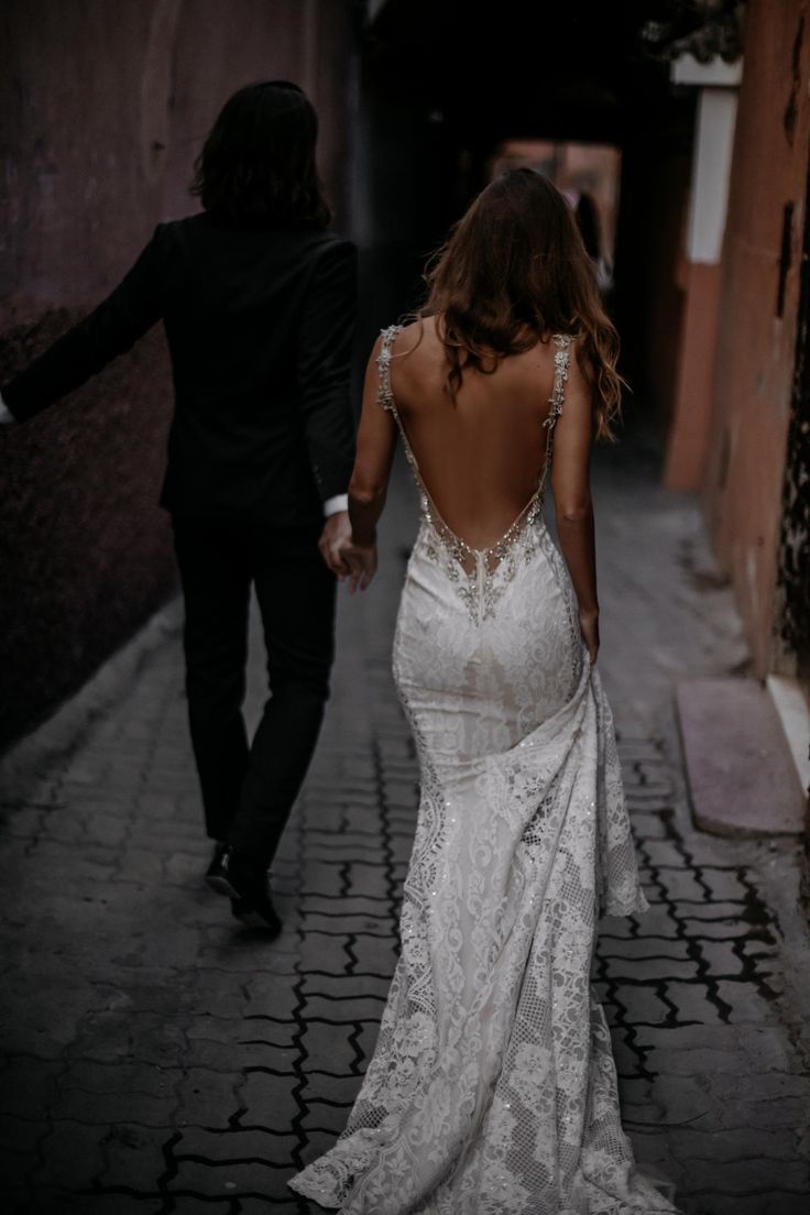 a woman in a white dress walking down a street next to a man in a tuxedo