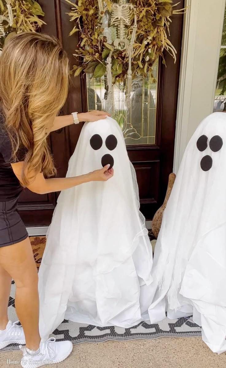 a woman standing next to two fake ghost heads in front of a door with their faces painted white