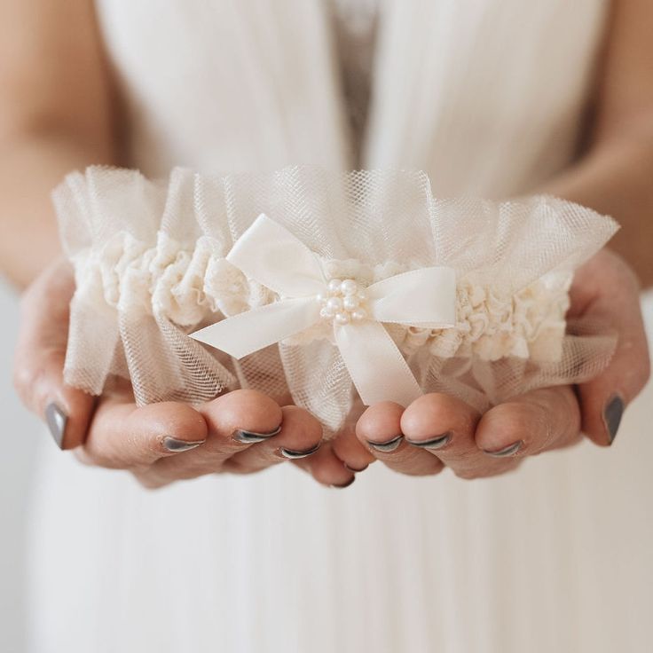 Cheers to the beautiful details of your wedding! When only the best will do. Our 'Heiress' style wedding garter heirloom is designed and detailed with the most delicate of laces, champagne lace, and detailed with hand sewn pearls, for the bride who has a special place in her heart for the finer things in life. Details Production Shipping Sizing Main Garter: Light ivory satin background with two layers of champagne tulle, a stripe of ivory lace and an ivory satin center tied bow with faux pearls Elegant White Bridal Accessories For Wedding Night, Bridal Accessories With Lace Trim For Ceremony, Elegant Fitted Bridal Accessories For Wedding Night, Elegant Fitted Tulle Bridal Accessories, Elegant Bridal Belt With Satin Bow For Wedding, Fitted Lace Bridal Belt For Ceremony, White Fitted Bridal Belt For Ceremony, Elegant Tulle Bridal Accessories For Bride, Elegant Bridal Accessories In Tulle