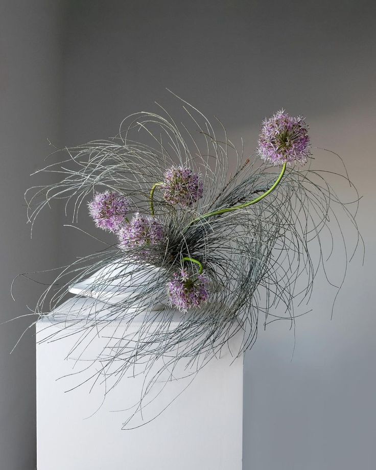 some purple flowers are sitting on top of a white pedestal in front of a gray wall