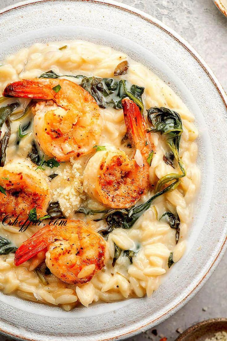 pasta with shrimp, spinach and cheese in a white bowl on top of a table