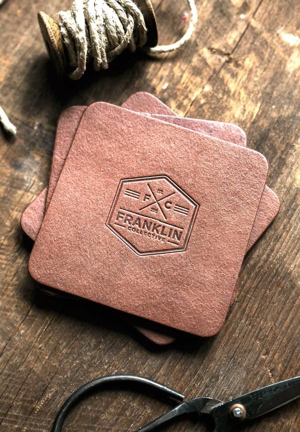 two pink coasters sitting on top of a wooden table next to yarn and scissors