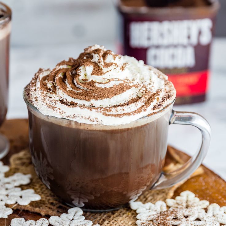 there is a cup of hot chocolate with whipped cream on top and coffee in the background