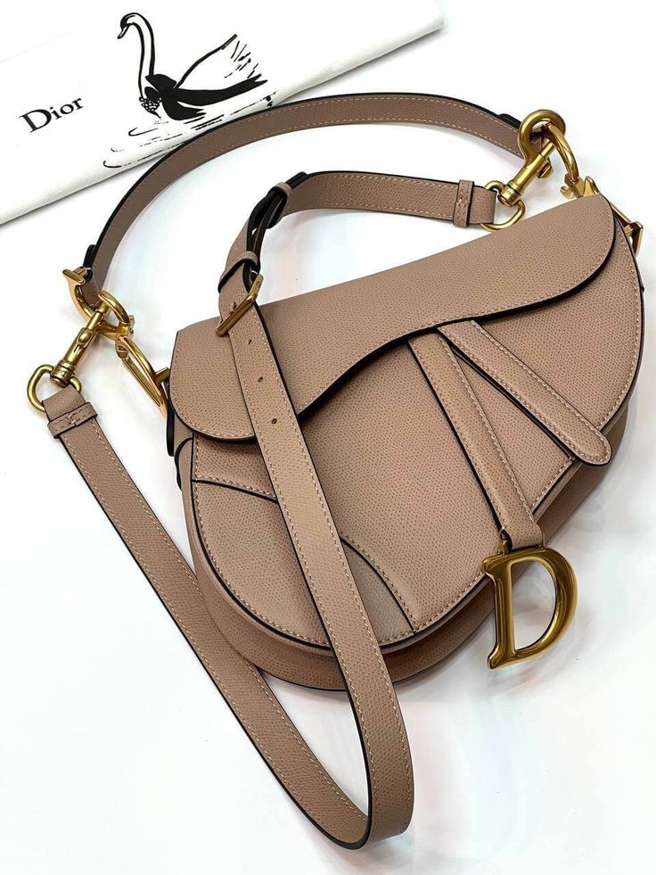 The iconic Saddle bag is reinvented once more by Maria Grazia Chiuri. Featuring a Saddle flap with a magnetic 'D' stirrup clasp, it boasts a 'CD' signature on each side of the handle. The black grained calfskin style is embellished with antique gold-finish metal hardware. The Saddle bag may be carried by hand or  over the shoulder and can be customized with different shoulder straps. SIZE AND FITDimensions: 25.5 x 20 x 6.5 cm.Belt length: 84-102 cm. Dior Saddle, Maria Grazia Chiuri, Belt Length, Maria Grazia, Hermes Handbags, How To Make Handbags, Purses Designer, Saddle Bag, Exclusive Bag