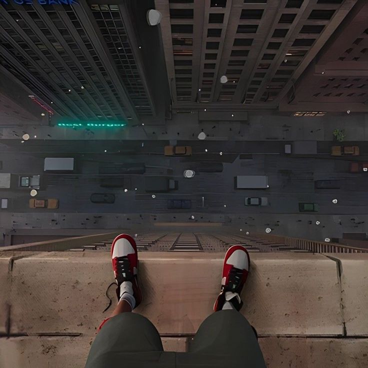 a person's feet with red and white sneakers standing on the edge of a building