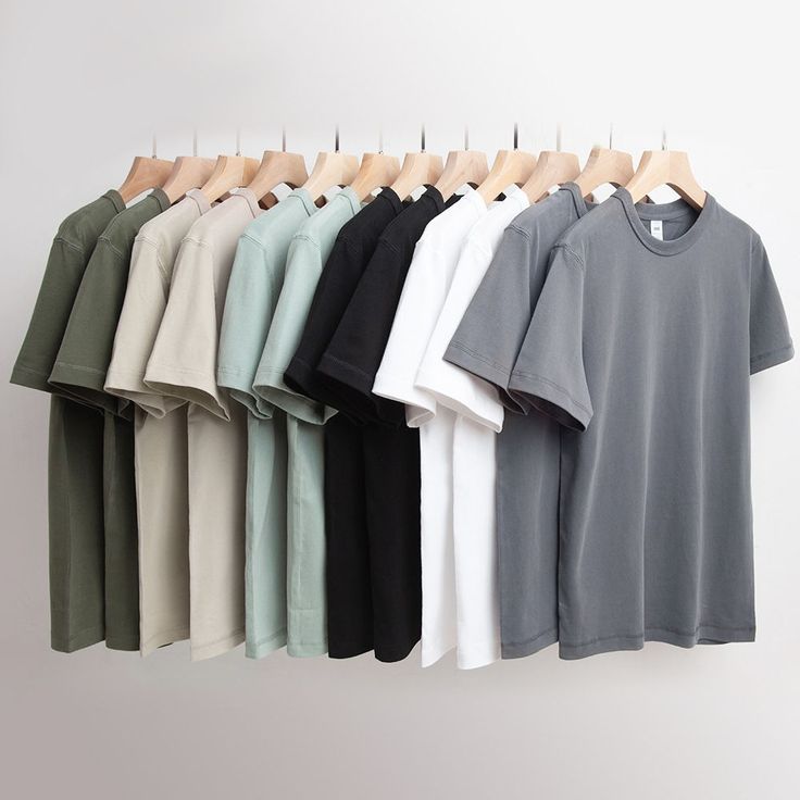 a row of t - shirts hanging on a clothes rack in front of a white wall