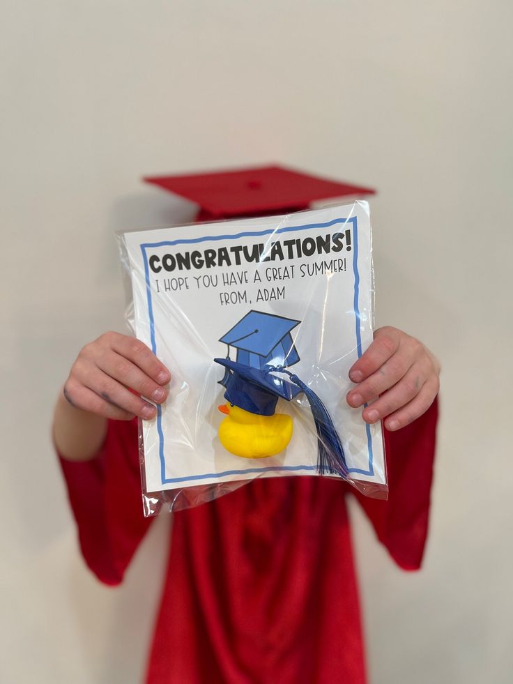 a person in a graduation gown holding up a rubber duck with congratulations written on it