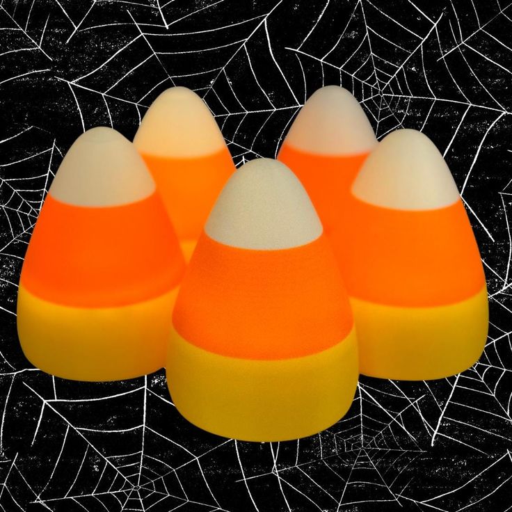 four orange and white candy corn on a black background with spiderwetche web