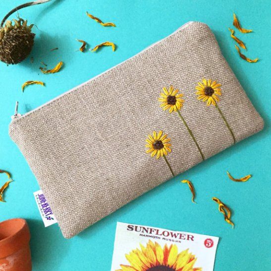 a sunflower embroidered onto a linen pouch next to some dried flowers and seed pods