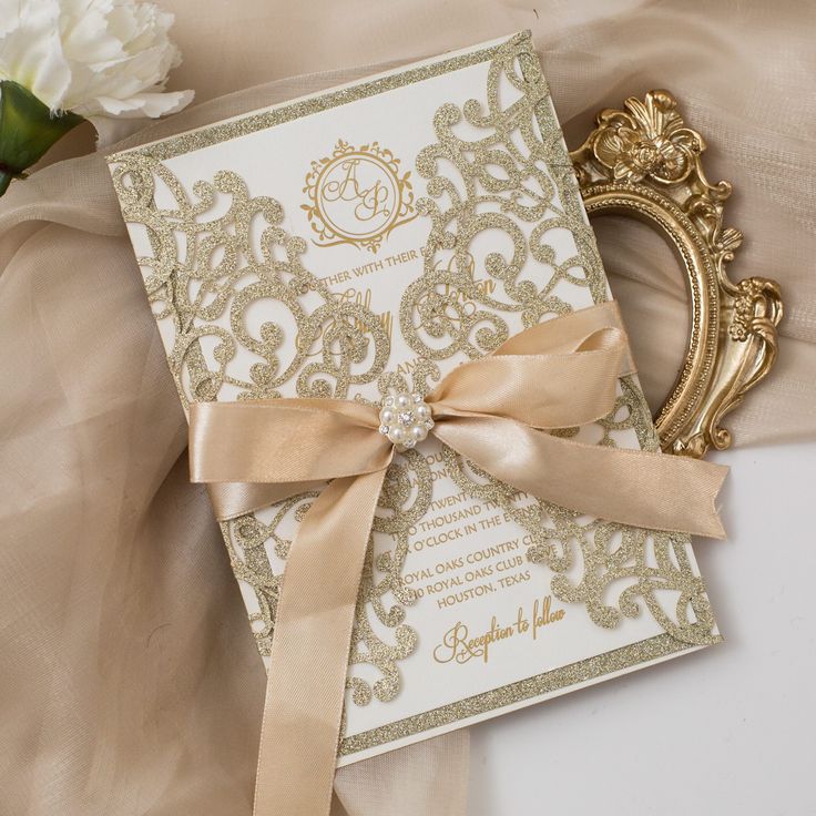 the wedding card is decorated with gold lace and a satin ribbon, along with a white flower