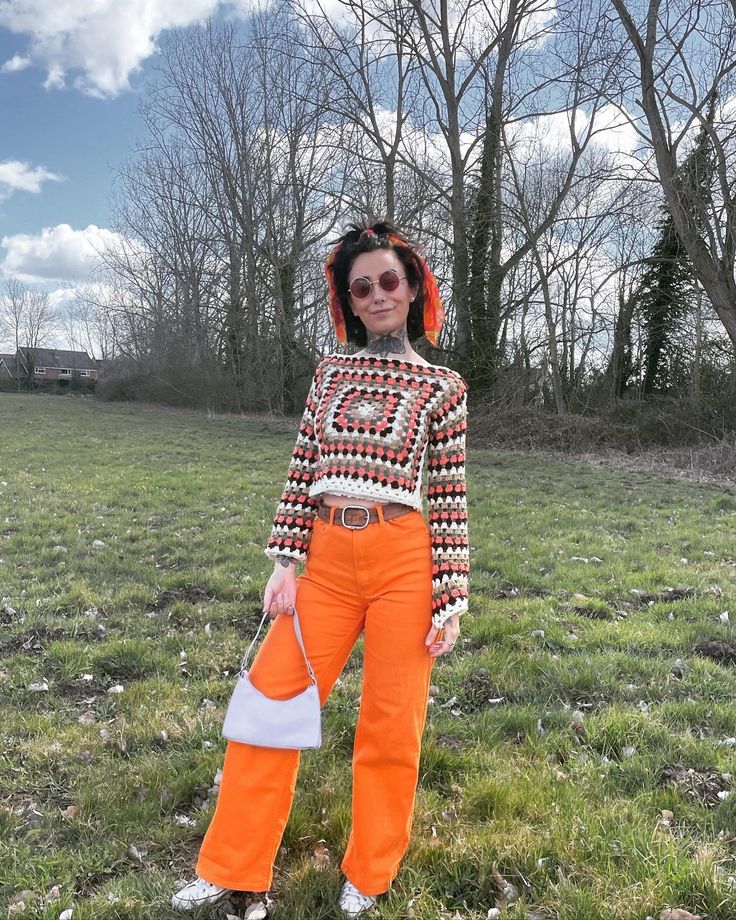 a woman in an orange outfit standing on top of a grass covered field next to trees