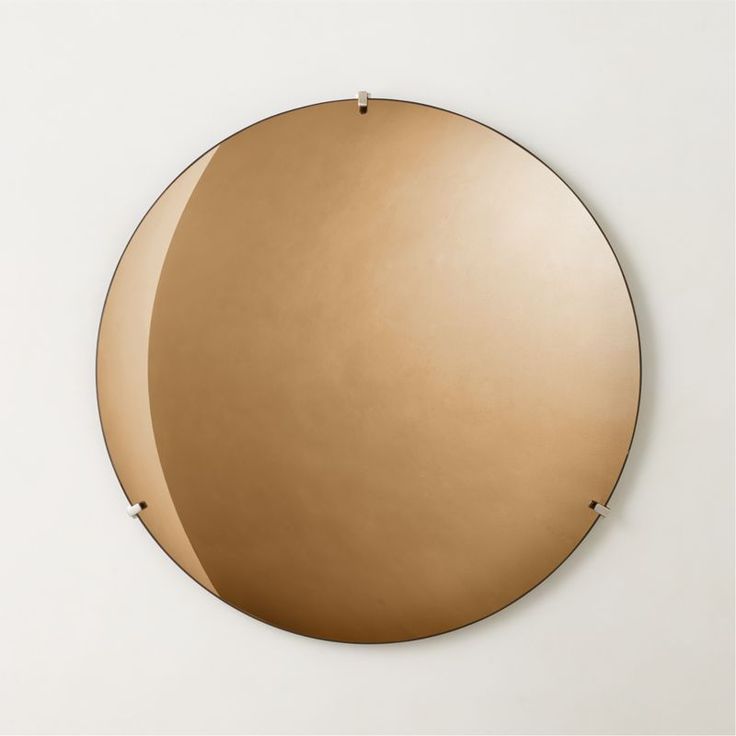 a round mirror hanging on the wall in front of a white wall with gold trim