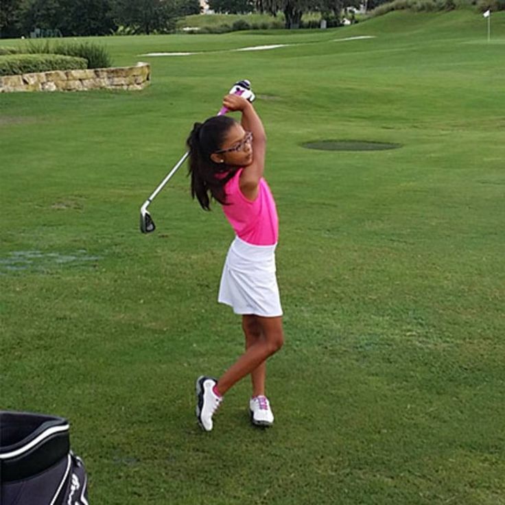 a woman in pink shirt and white skirt hitting a golf ball on the green field