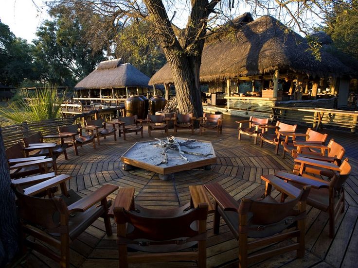 an outdoor seating area with wooden chairs and tables in front of thatched roof huts