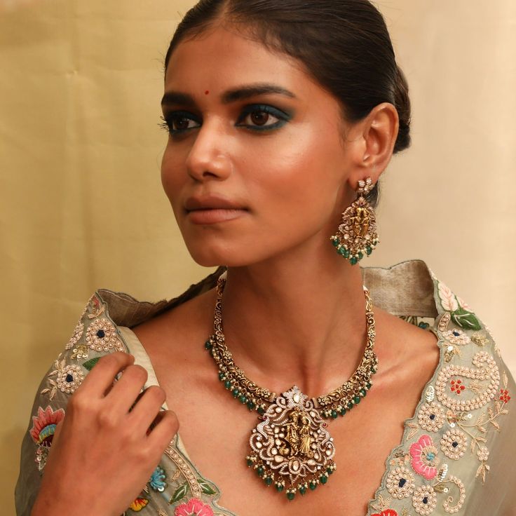 Description Indulge in the elegance of the Vrindavana hasli necklace set. Inspired by the rich jewelry heritage of India, this hasli features sparkling moissanite stones and temple art motifs. The central medallion showcases an intricate Radha Krishna idol, surrounded by exquisite peacock and floral patterns. Crafted with 925 silver with Victorian plating & finished with semi-precious emerald beads and cluster pearl drops, this necklace exudes a vintage charm. Product Information Materials used: Radha Krishna Idol, Rich Jewelry, Hasli Necklace, Krishna Idol, Art Motifs, Victorian Pendants, Temple Art, Emerald Bead, Moissanite Jewelry