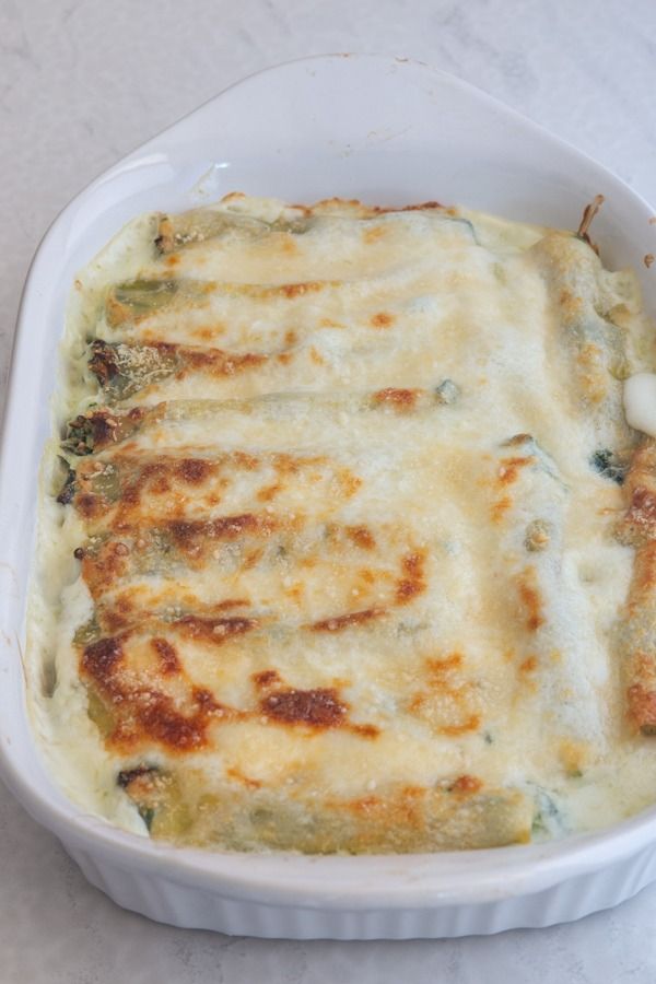 a casserole dish with cheese and spinach in it on a white surface