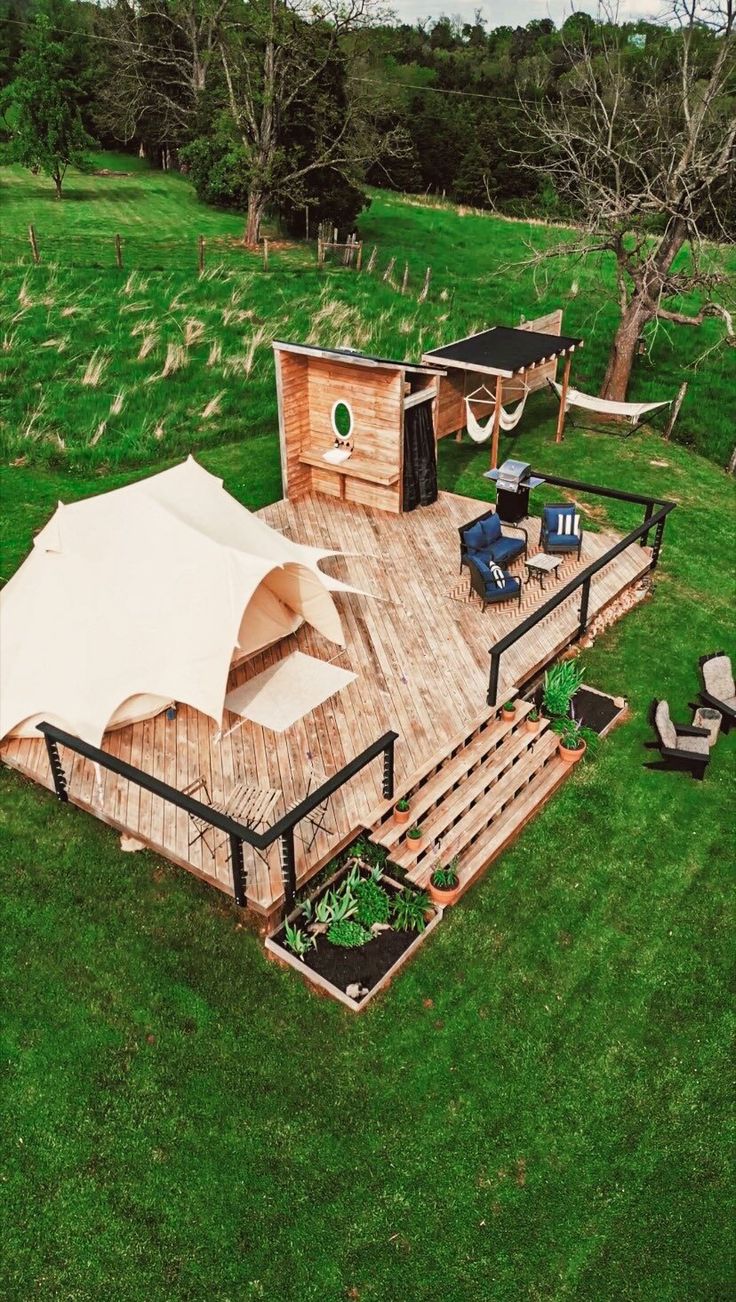 an aerial view of a wooden deck in the middle of a grassy area with chairs and umbrellas