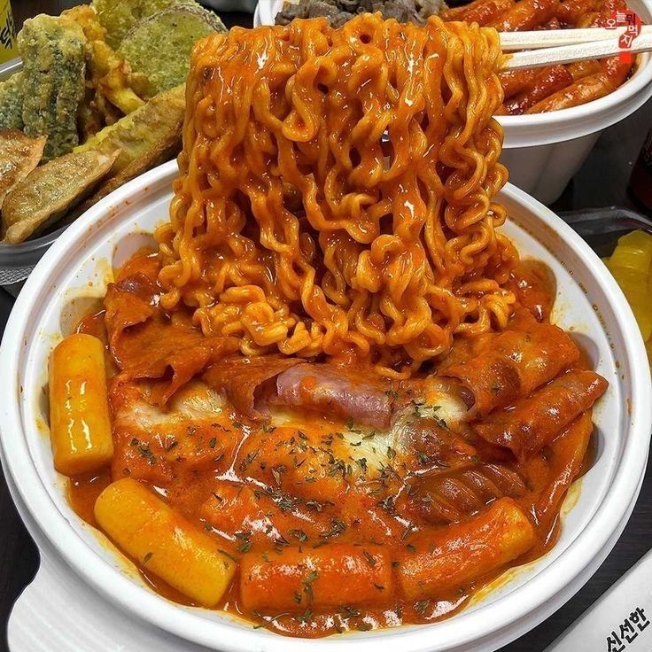 a bowl filled with noodles and meats on top of a table next to other dishes