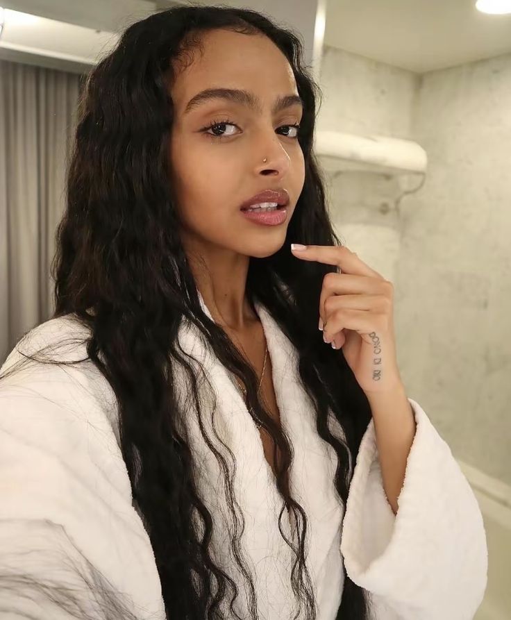 a woman in a bathrobe brushing her teeth and looking at the camera with an intense look on her face