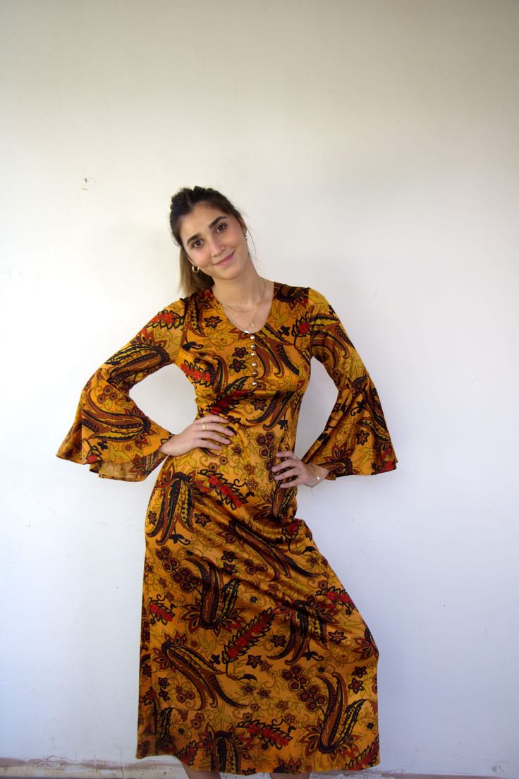 "A stunning vintage maxi dress in a floral psychedelic print in vibrant shades of orange, brown, yellow, red, and black. The dress features bell sleeves, an empire waist, and decorative gold buttons embellishing the upper front. It fastens with a back zipper and is made of shiny polyester material.   aside from minor signs of wear, good vintage condition, clean ready to wear.  ** Model is 5'7\" and size S** Approximate size: S - please refer to the measurements. M E A S U R E M E N T S -were taken with garments laying flat, please double where necessary. ------------------------♥-------- bust: 16.5\"-42cm empire waist:14\"-72cm Length: 51\"-130cm ----------------------------------------- All items are vintage pieces, previously loved They may show natural signs of wear & and age. I do my b Empire Waist Maxi, 1970s Dress, 1970s Dresses, Vintage Maxi Dress, Bell Sleeve Dress, Shades Of Orange, Orange Brown, Brown Orange, Dress Vintage