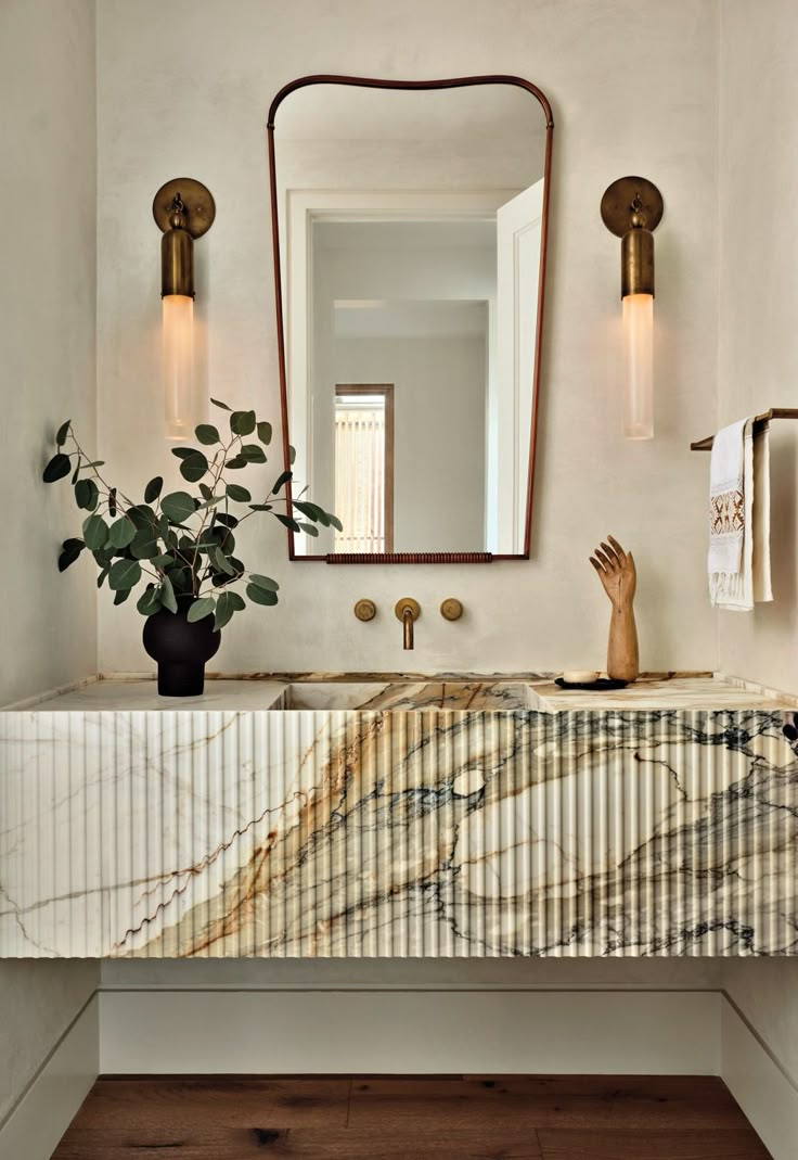 a bathroom sink with marble counter top next to a mirror and plant in the corner