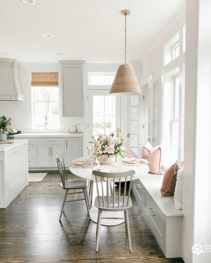 a kitchen with white cabinets and wooden flooring next to a dining room table surrounded by chairs