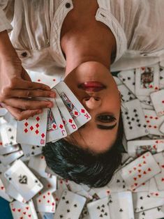 a woman holding playing cards in her hands while laying on the ground with other playing cards