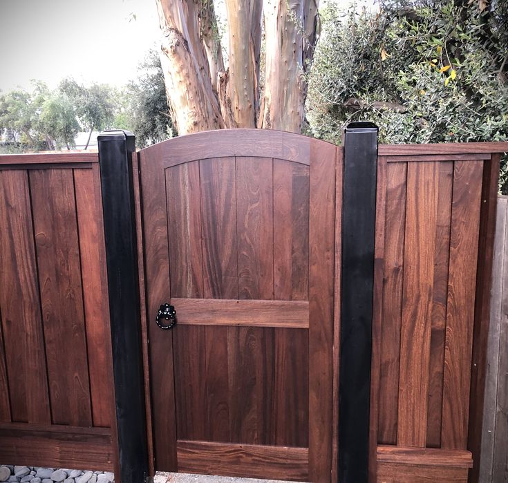 a wooden gate with two black iron posts and a tree in the backround