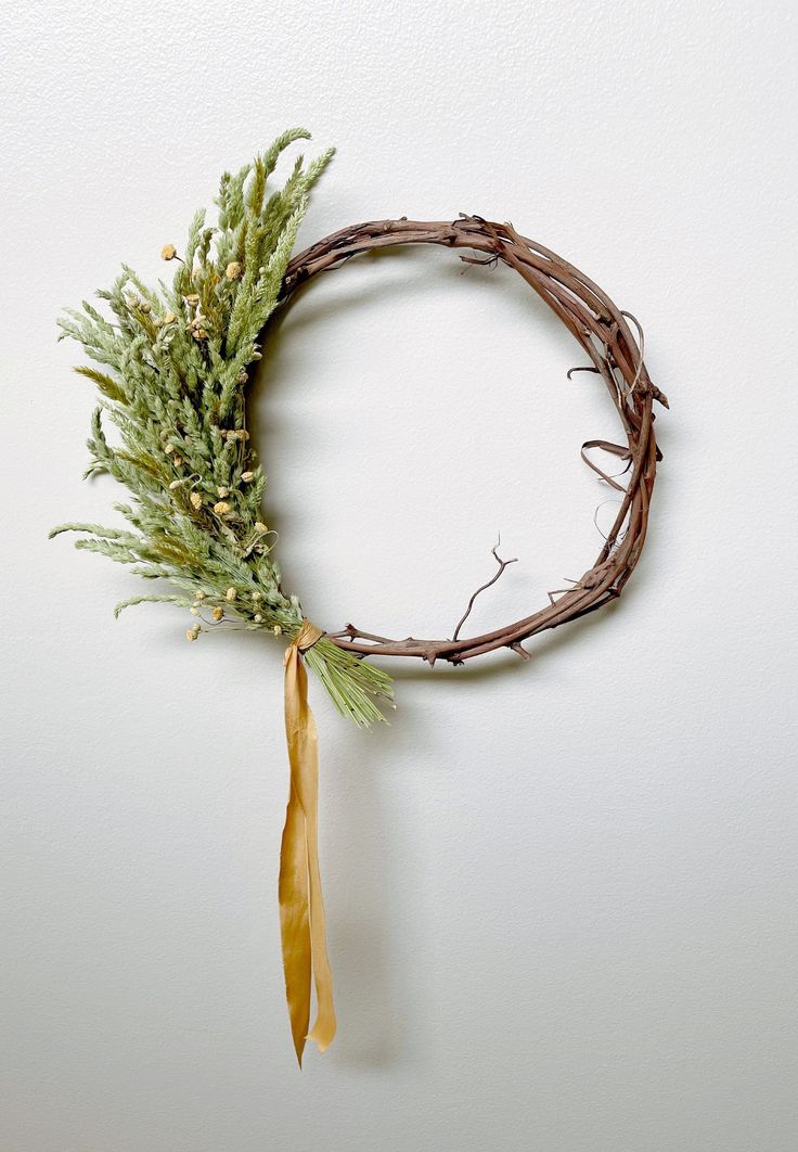 a twig wreath is hung on the wall with a yellow ribbon and some branches