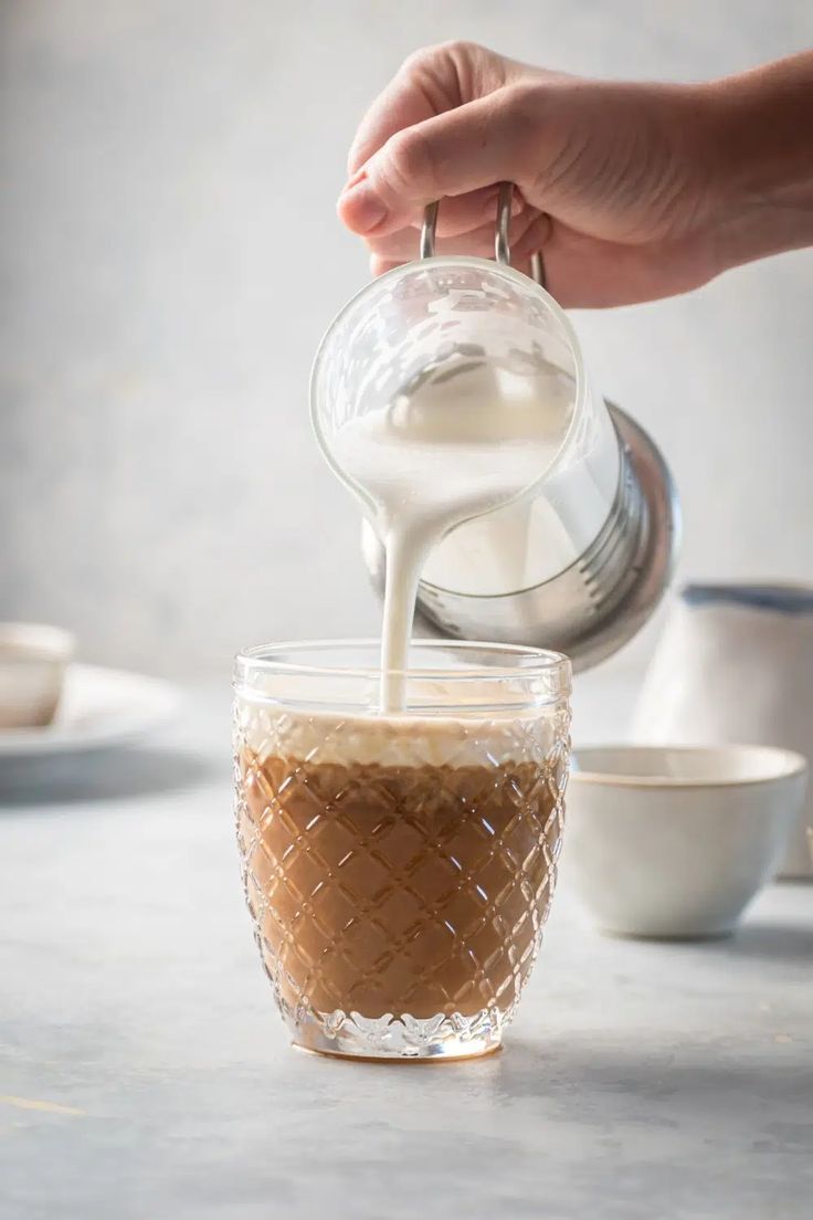 a person pouring milk into a glass cup