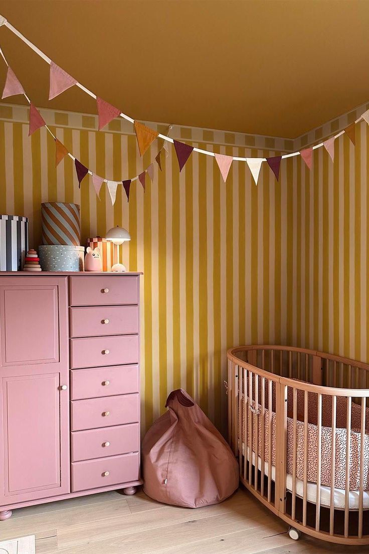 a baby's room with pink furniture and striped wallpaper, including a crib