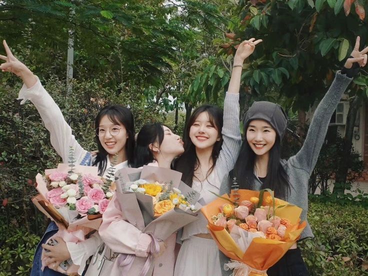 three girls are posing with flowers and giving the peace sign while one girl is holding her hand up