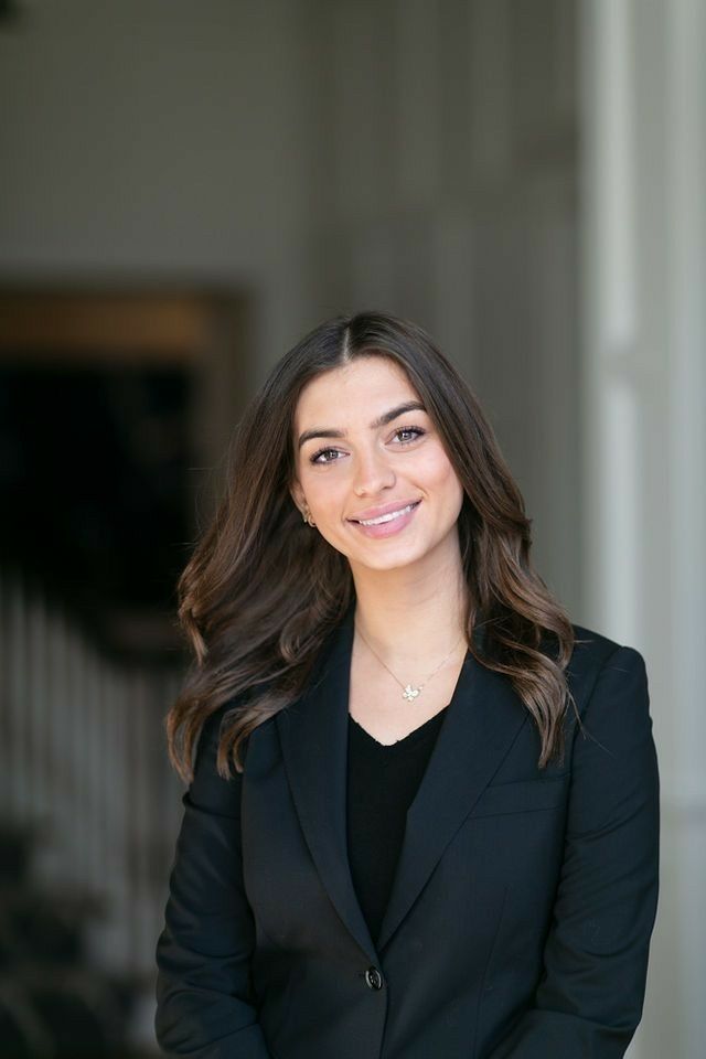 a woman wearing a black suit and smiling at the camera with her hands in her pockets