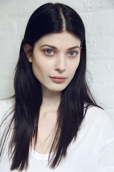 a woman with long black hair wearing a white t - shirt and looking at the camera